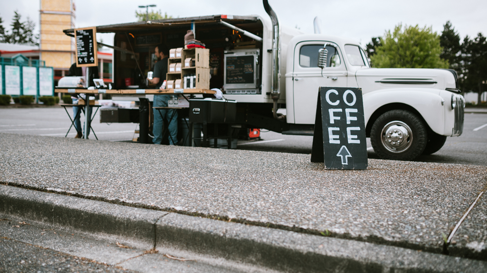 A coffee truck owners stands and serves coffee.